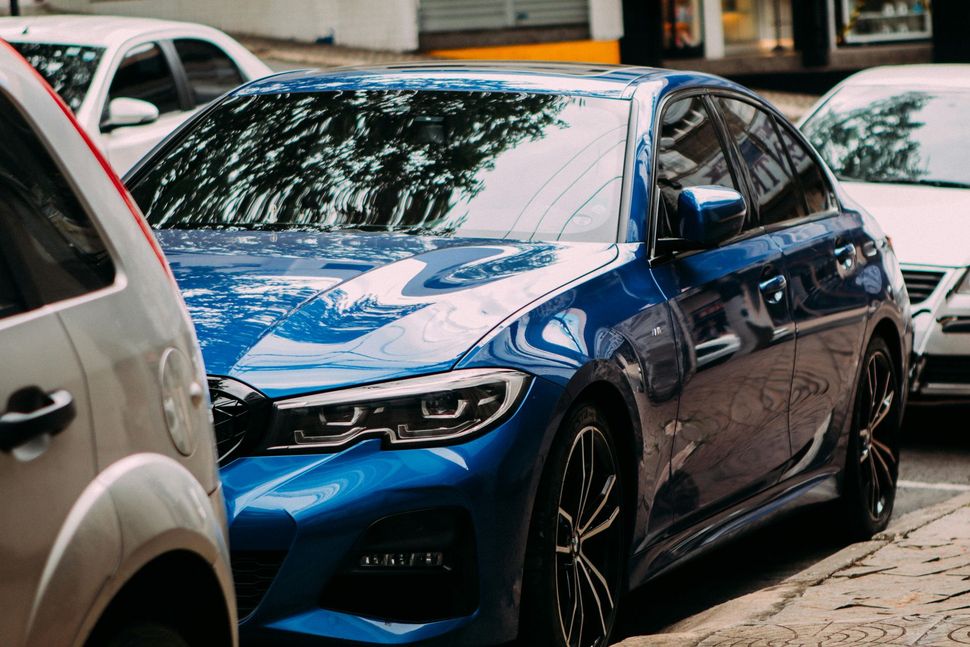 Blue sedan parked on a city street, partially obscured by other cars.