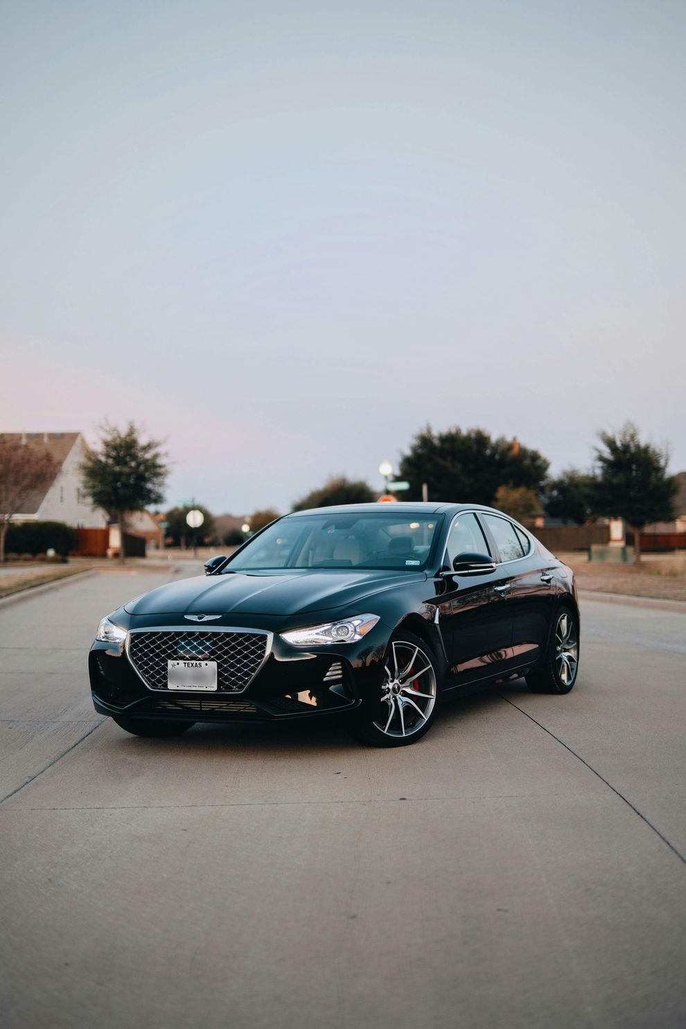 Black Genesis G70 sedan parked on a residential street at dusk.
