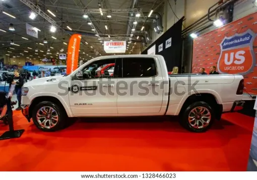 Blue Volvo semi-truck with white trailer parked on gravel. Buildings in the background.