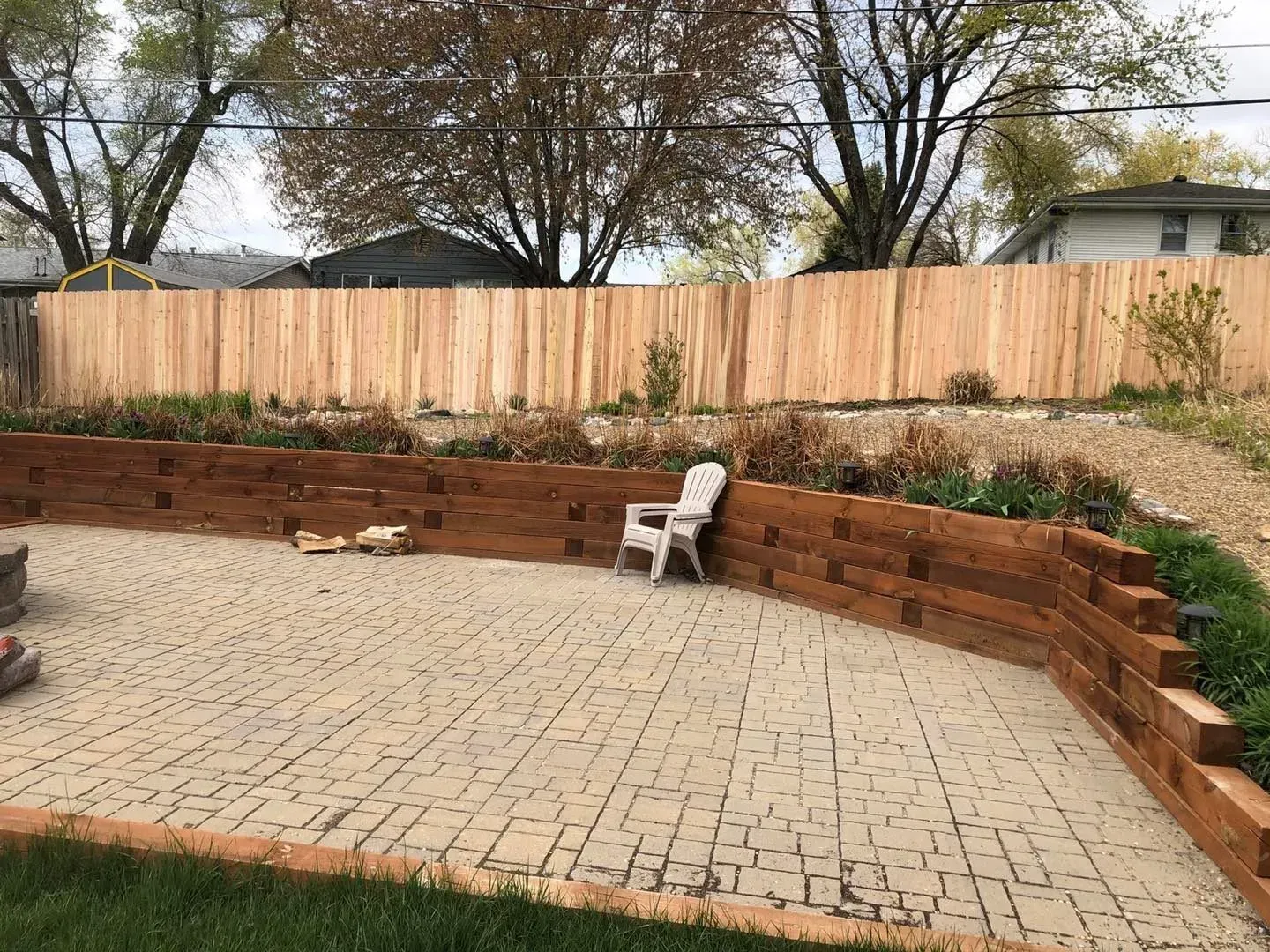 Stone patio with a retaining wall and wooden fence, a white chair sits on the patio.