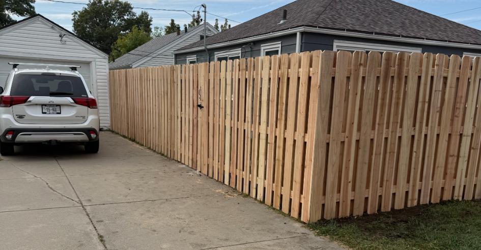 SUV parked in driveway next to a wooden privacy fence and a garage; a house is in the background.