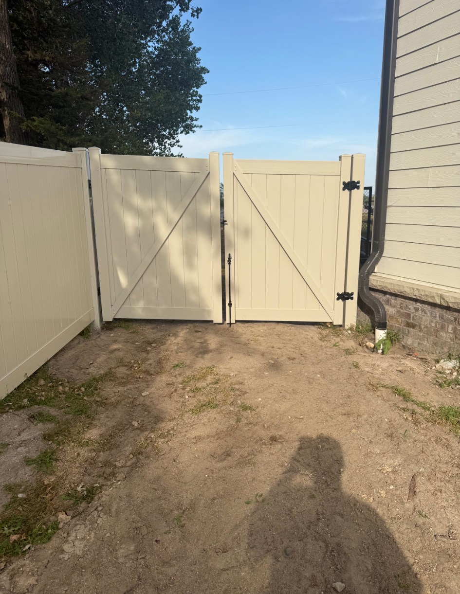 Tan double gate in a matching fence, leading to a sandy area.