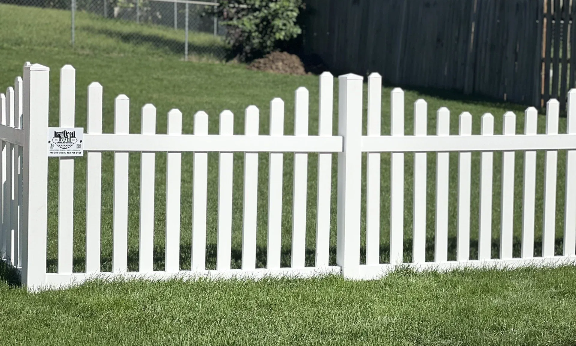 White picket fence in a grassy yard, with rounded top pickets.