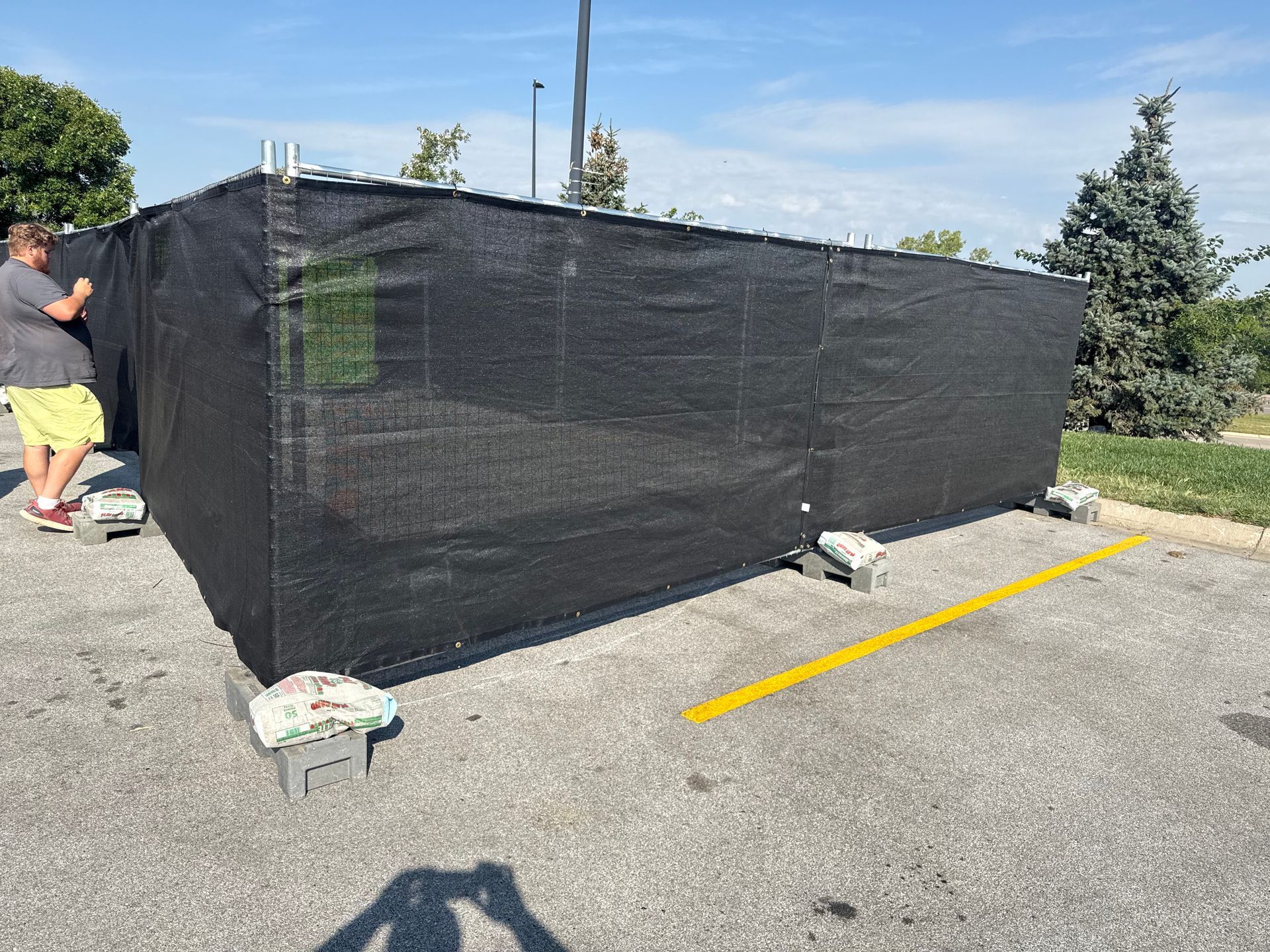 A temporary black fence in a parking lot. A person adjusts the fence. Sunny day.