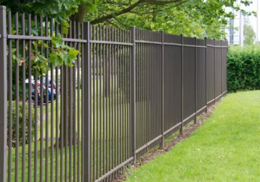 Brown metal fence bordering green grass.