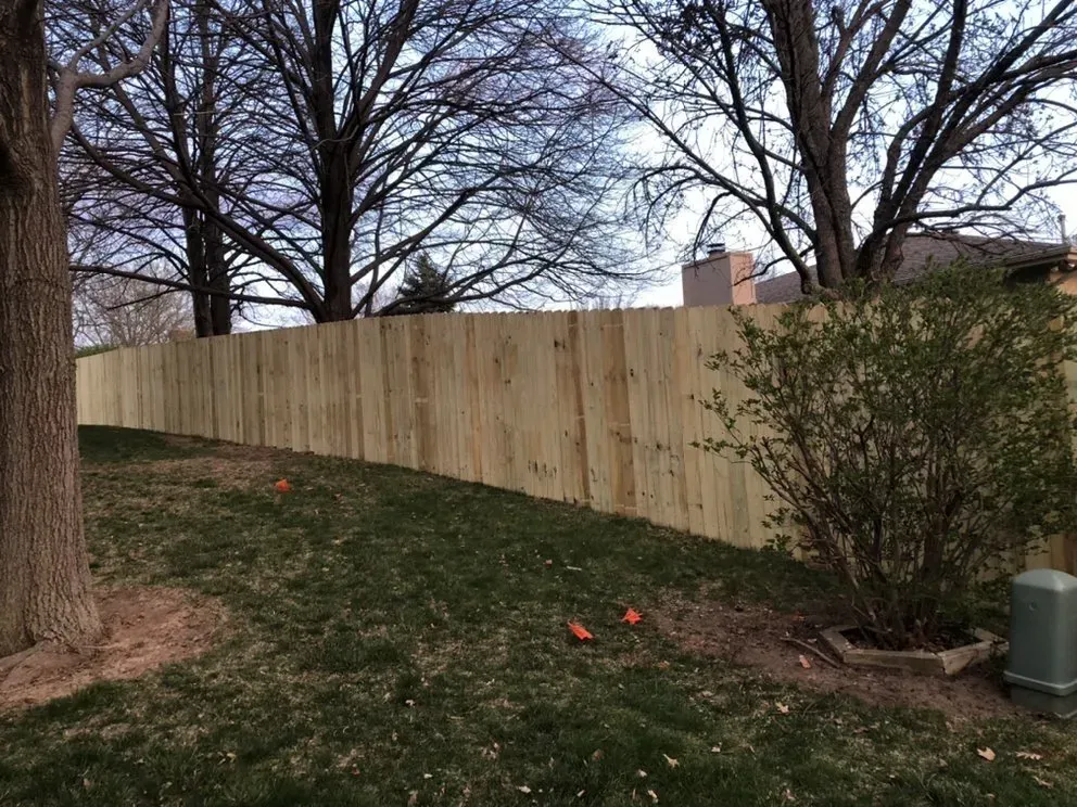 Wooden fence on a slight hill, with grass and trees in the background. Cloudy sky.