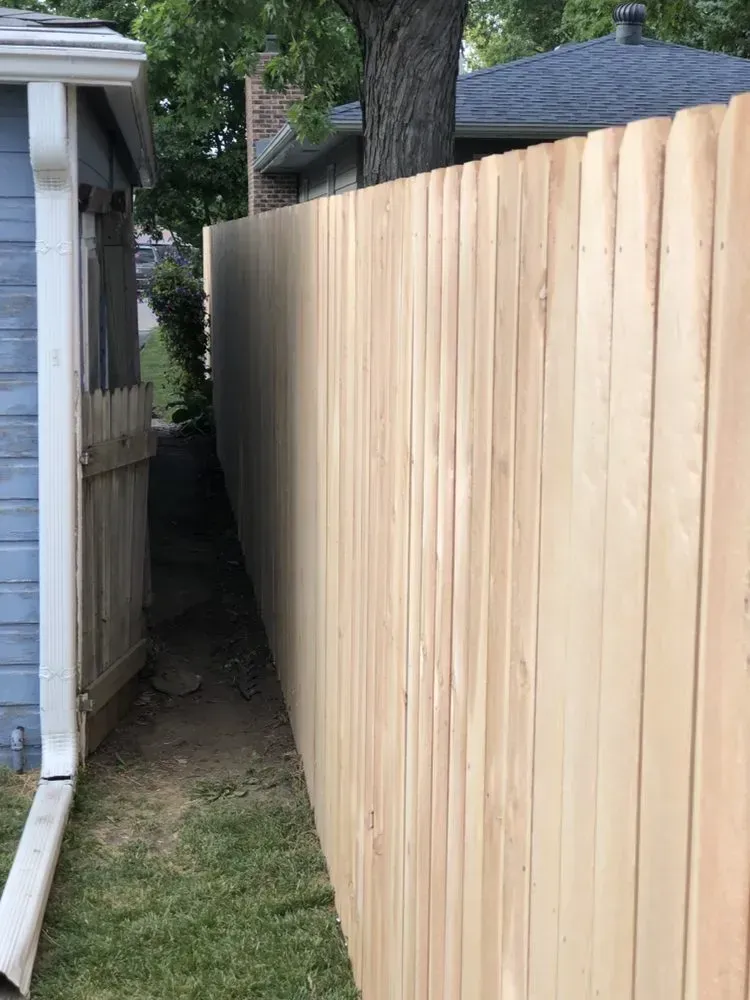 Wooden fence running along side a building and narrow yard.