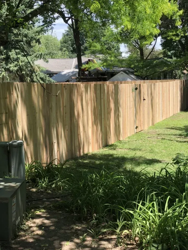 Wooden privacy fence in a grassy yard, sunlight casts shadows.