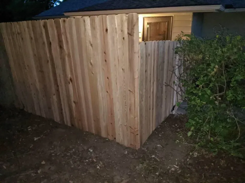 Wooden fence corner next to a green bush and a house.