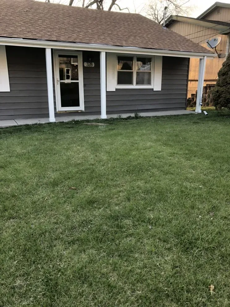 Gray house with white trim, brown roof, and green lawn.