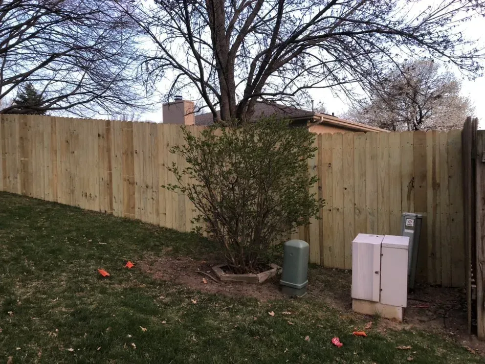 Wooden fence in backyard, shrub and utility boxes in front of it.