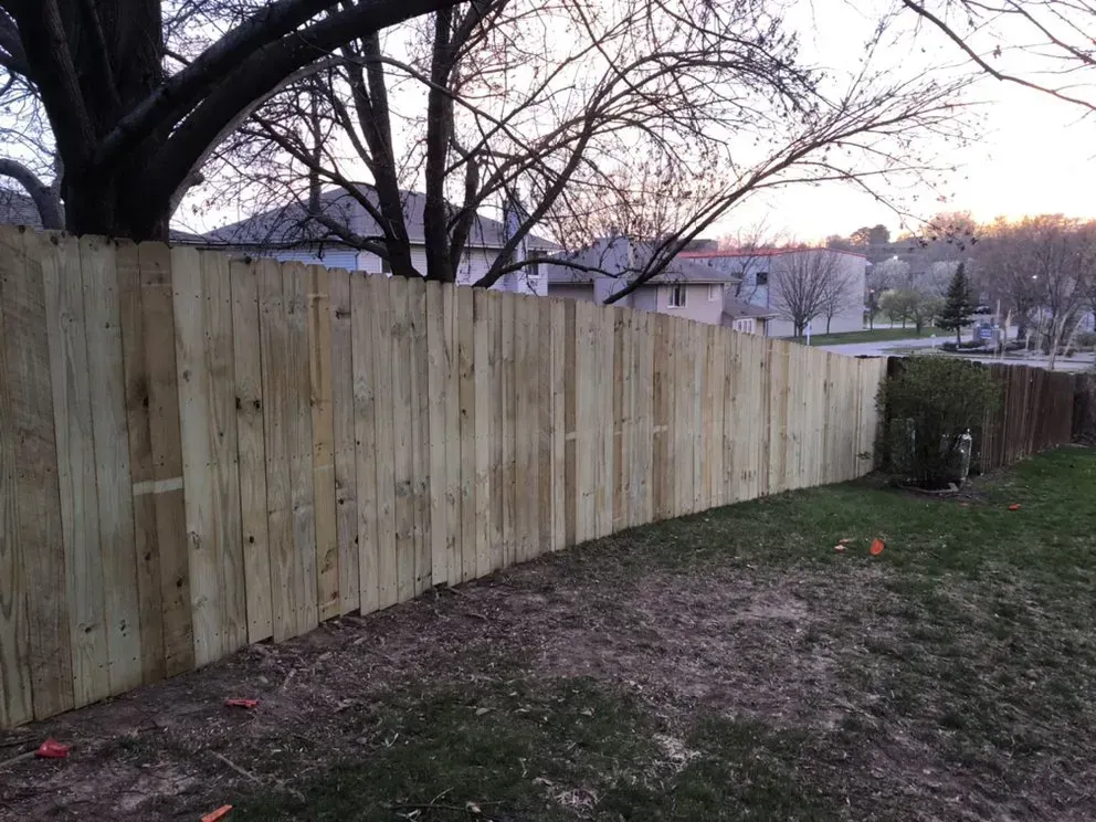 Wooden fence curving through a yard, with houses and trees in the background.