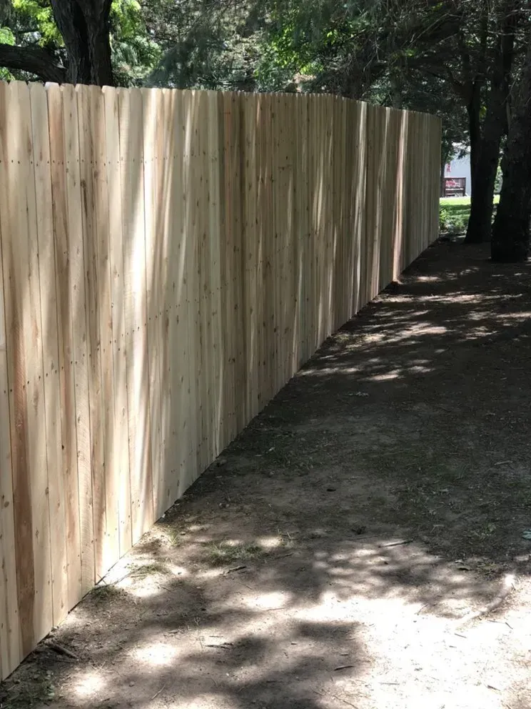 Wooden fence curving along a path. Sunlight casts shadows on the wooden planks.