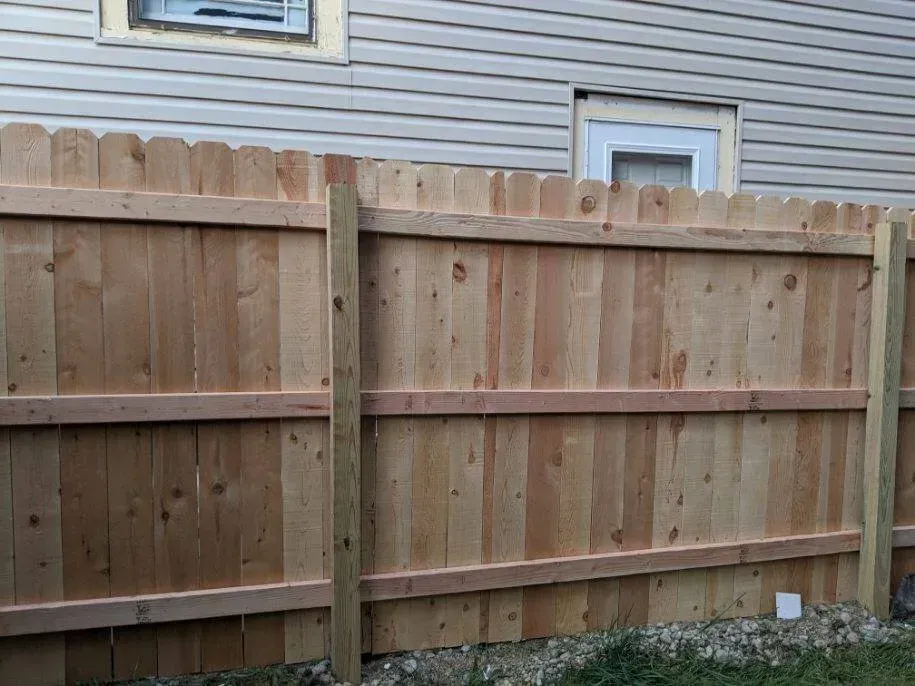 Wooden fence in front of a house, consisting of vertical planks and horizontal rails.