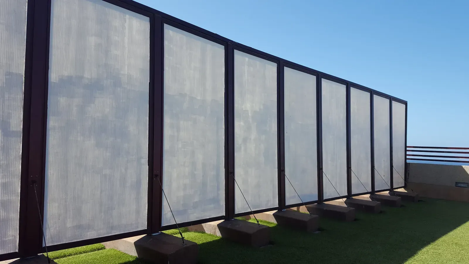 Outdoor wall with rectangular panels of mesh material, brown framing, green grass, and blue sky.