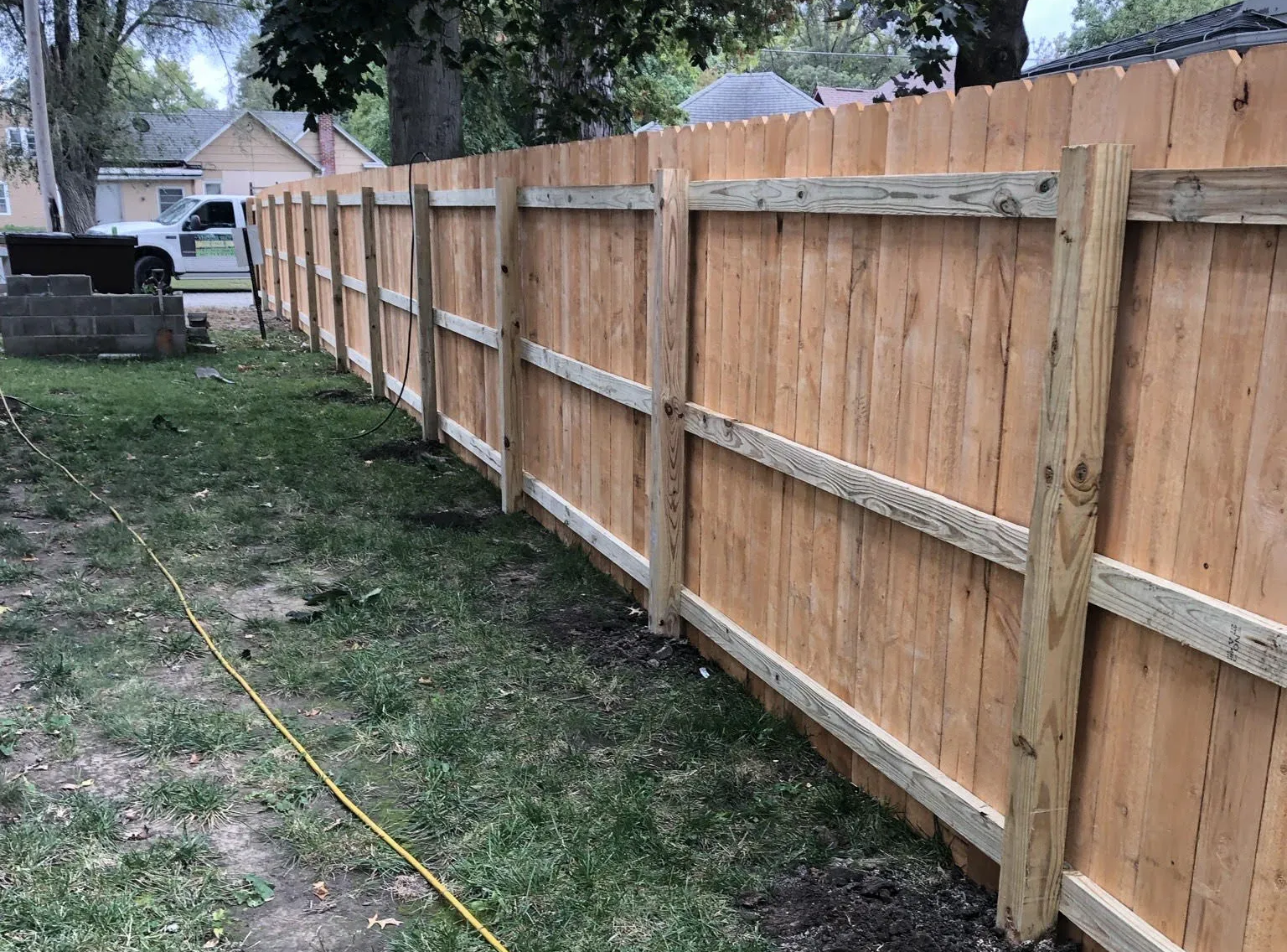 Wooden fence in a grassy yard, framing a property. Brown wood, cloudy sky, residential setting.