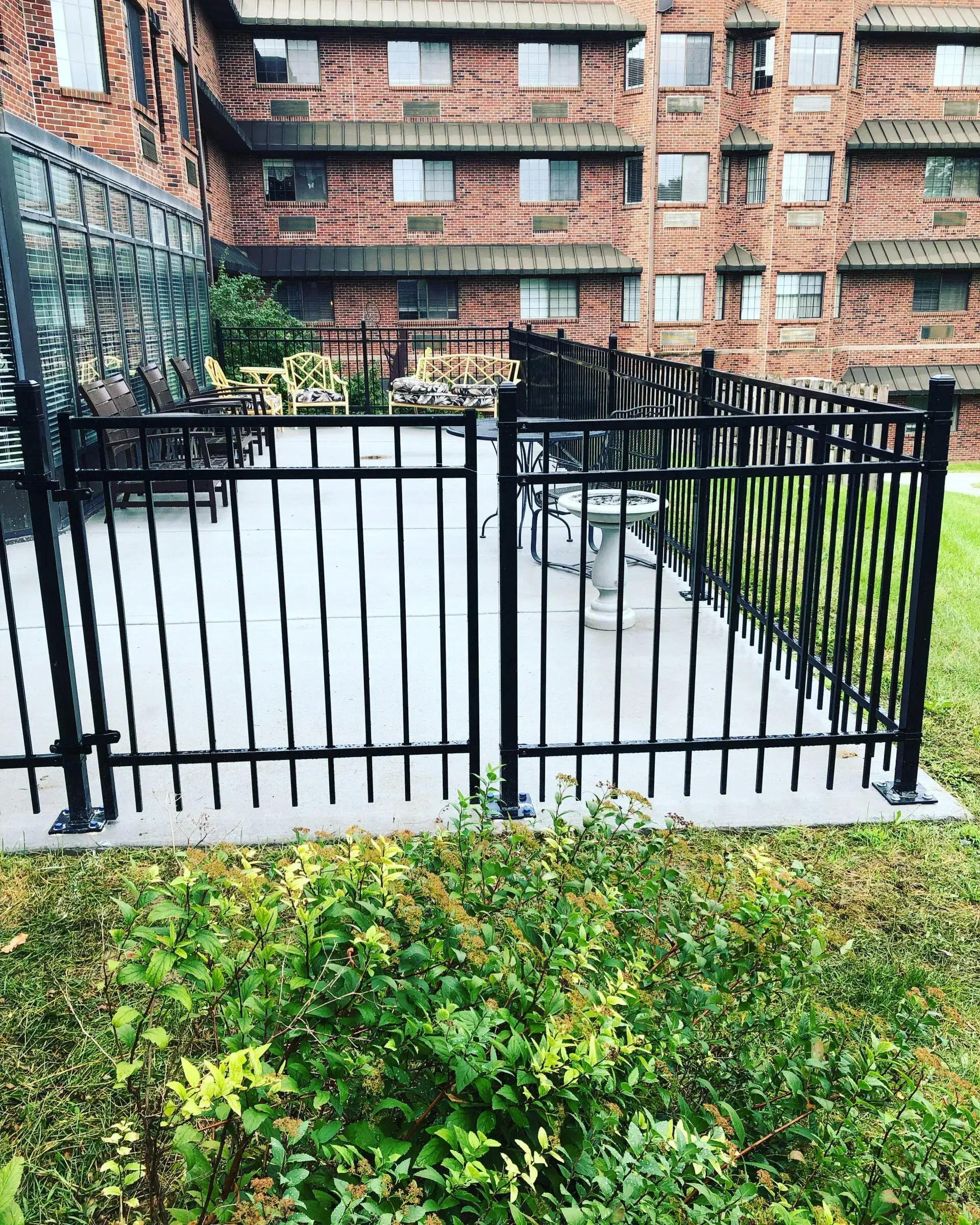 Black metal fence surrounding a concrete patio area in front of a brick building.