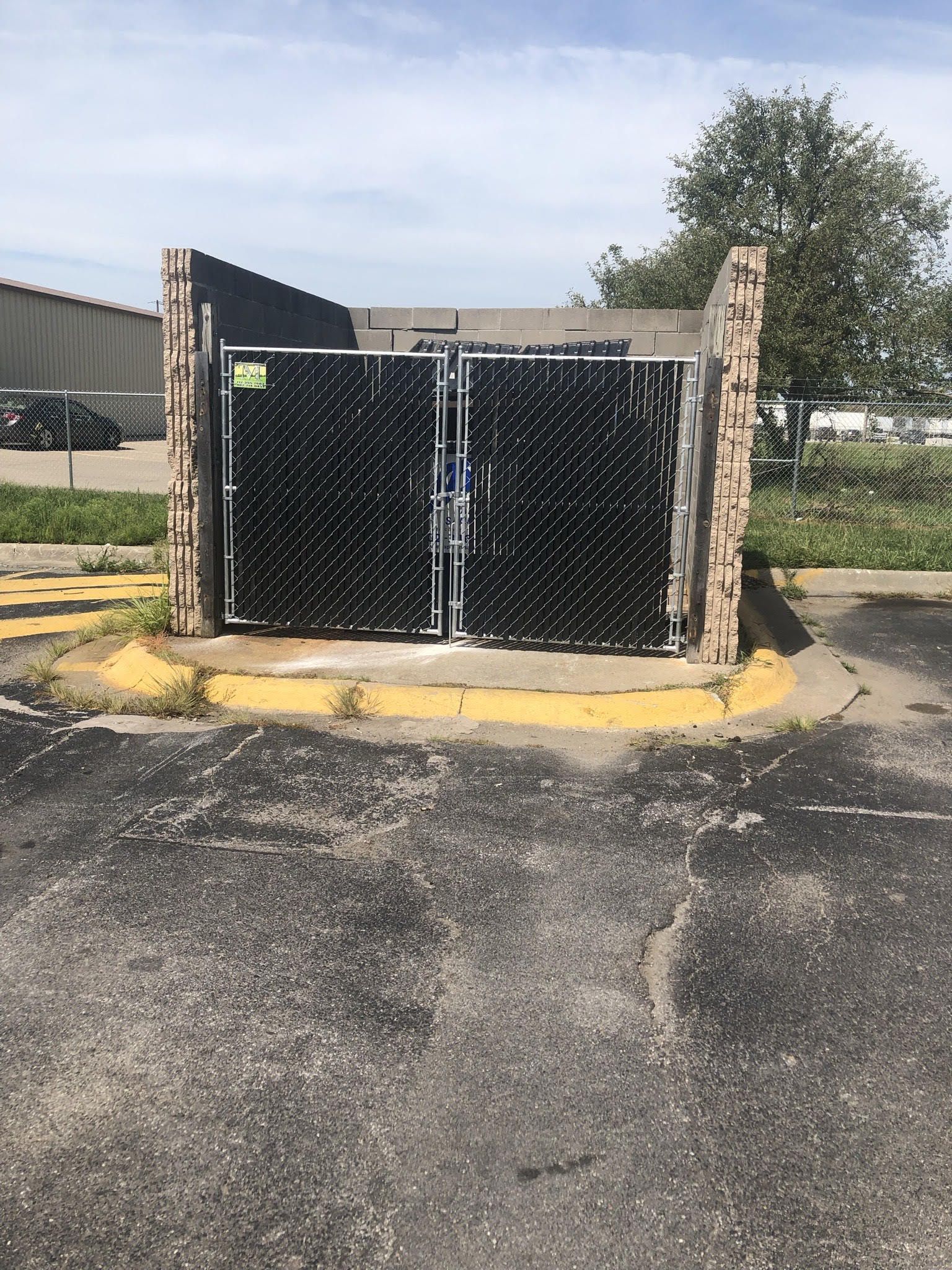 Black trash enclosure with gate in a parking lot, brick columns, yellow curb.