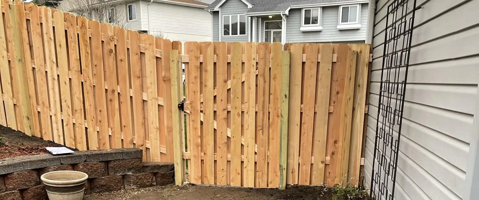 Wooden fence with gate in front of a house, next to a siding wall.