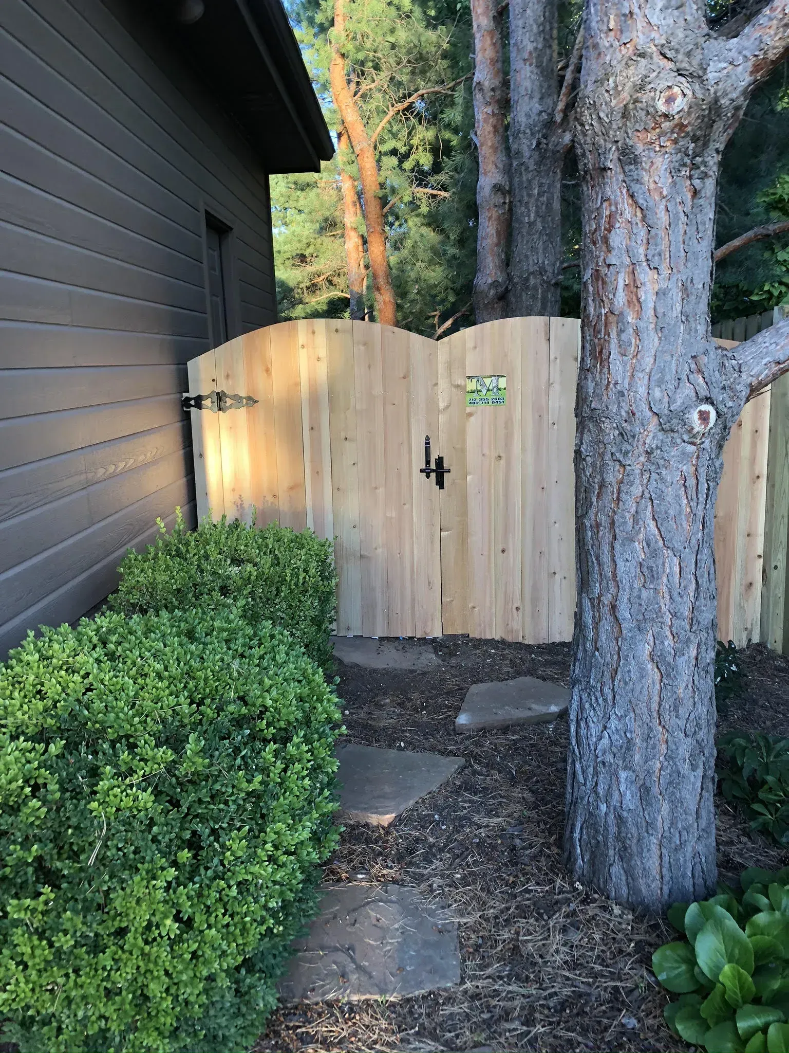 Wooden gate between a building and a tree, with stepping stones leading to it.