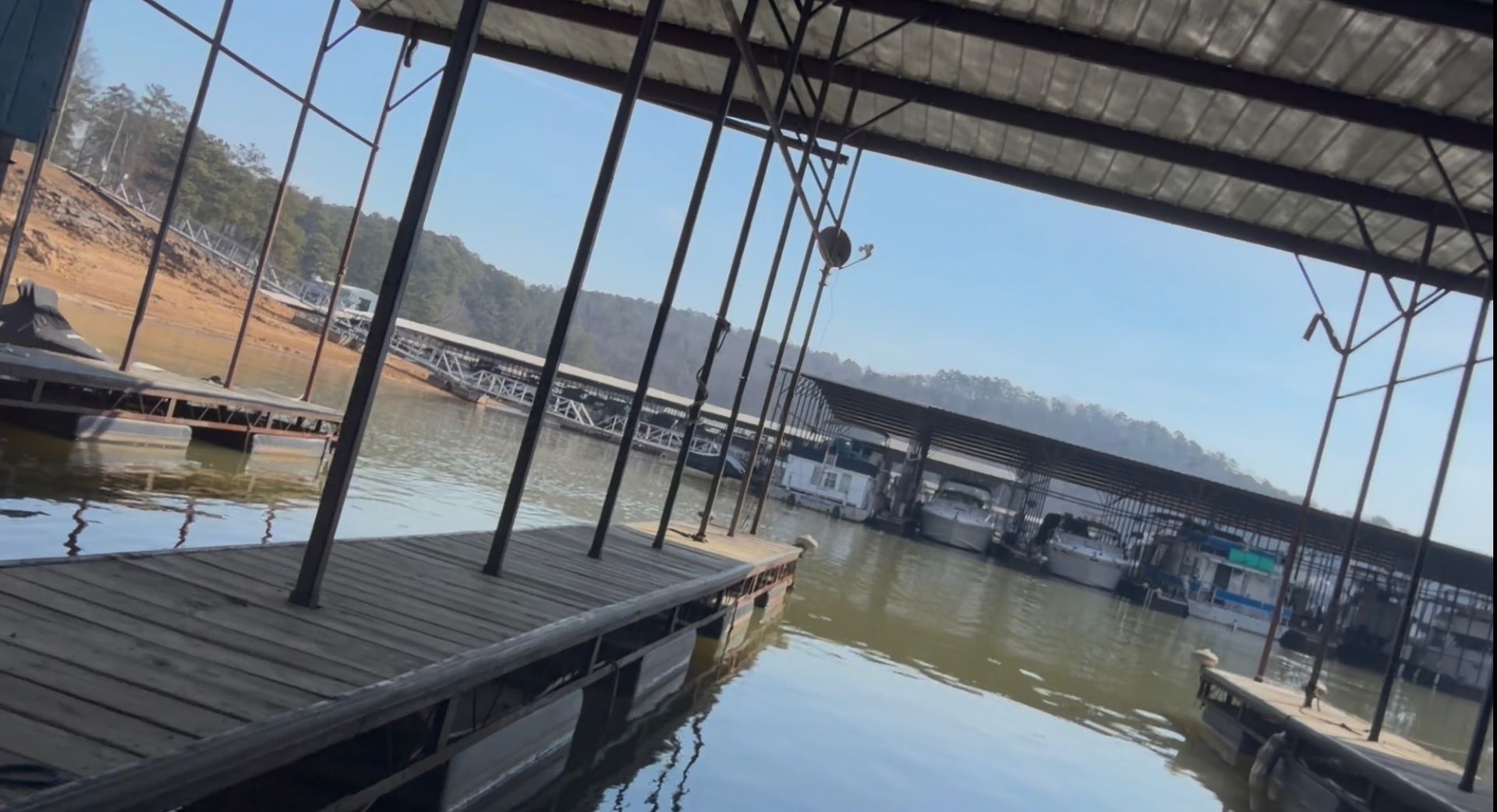 Man in hard hat and safety vest working on electrical box on a dock at sunset. Boat and lake visible.