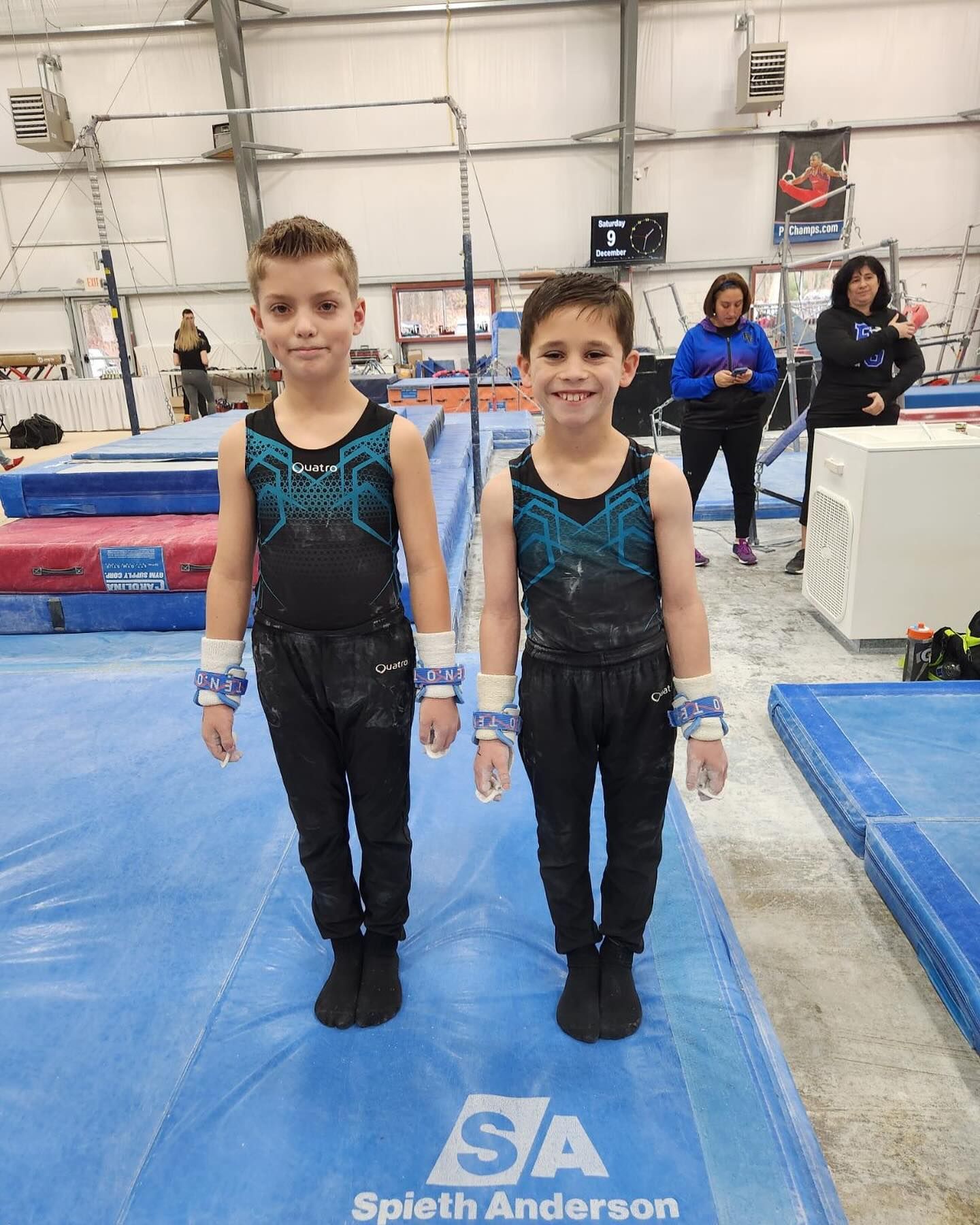 Two young boys are standing next to each other on a gymnastics mat.