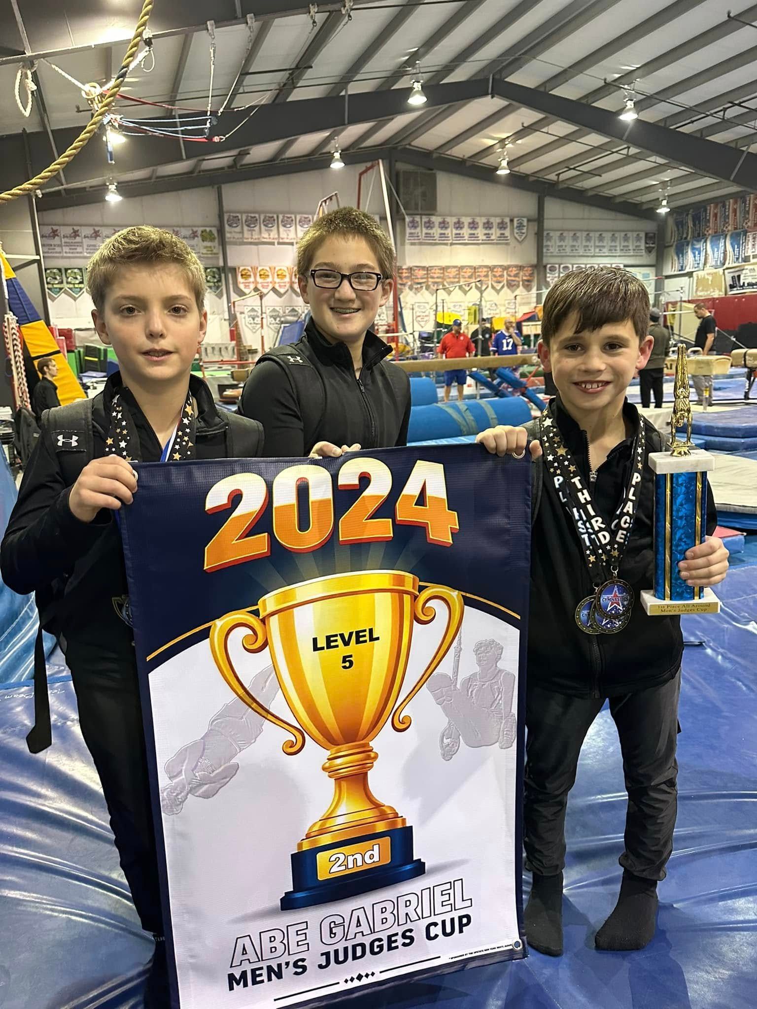 Three young boys wearing medals are standing next to each other on a gym floor.