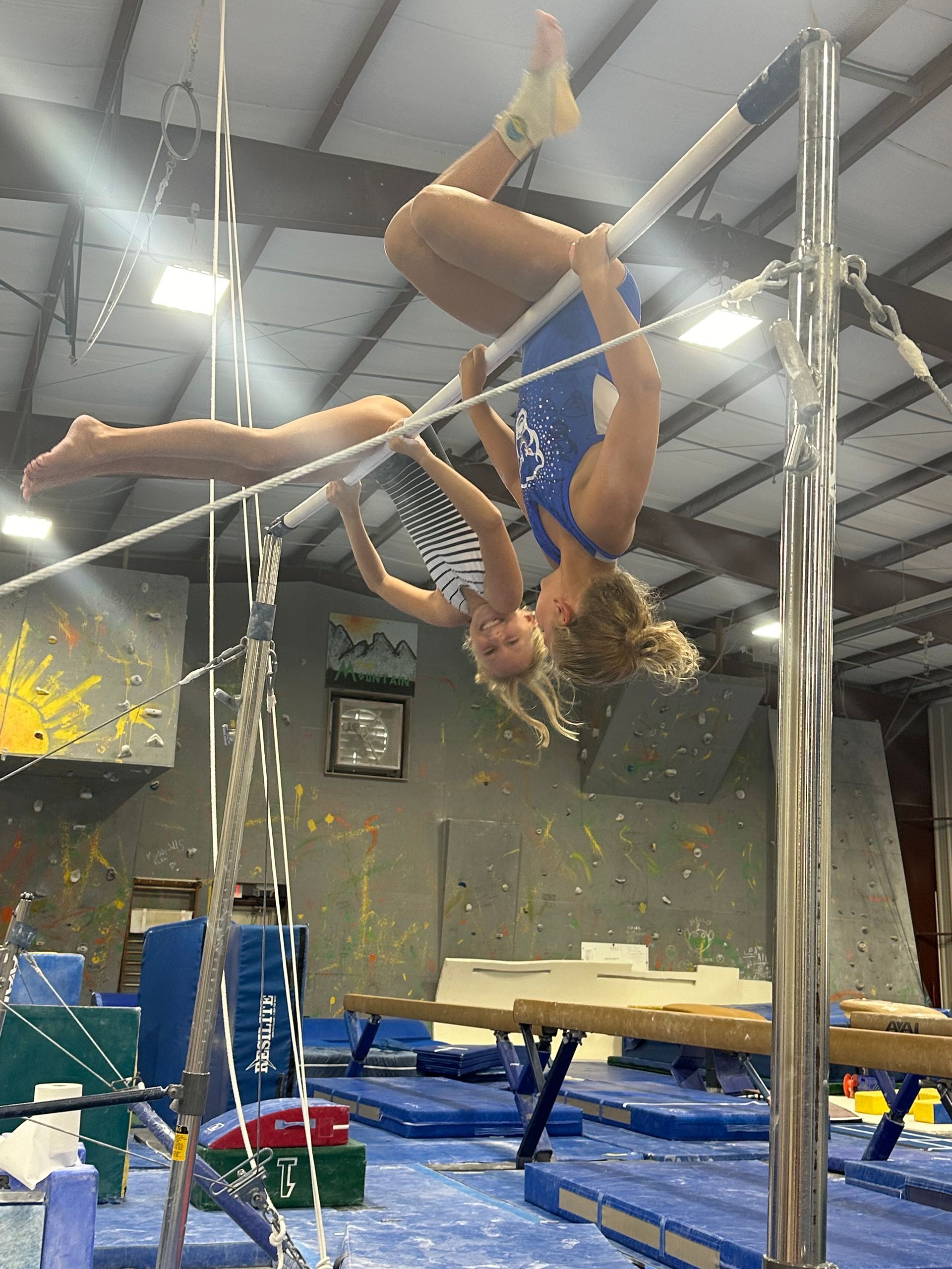 A woman is doing a handstand on a bar in a gym.