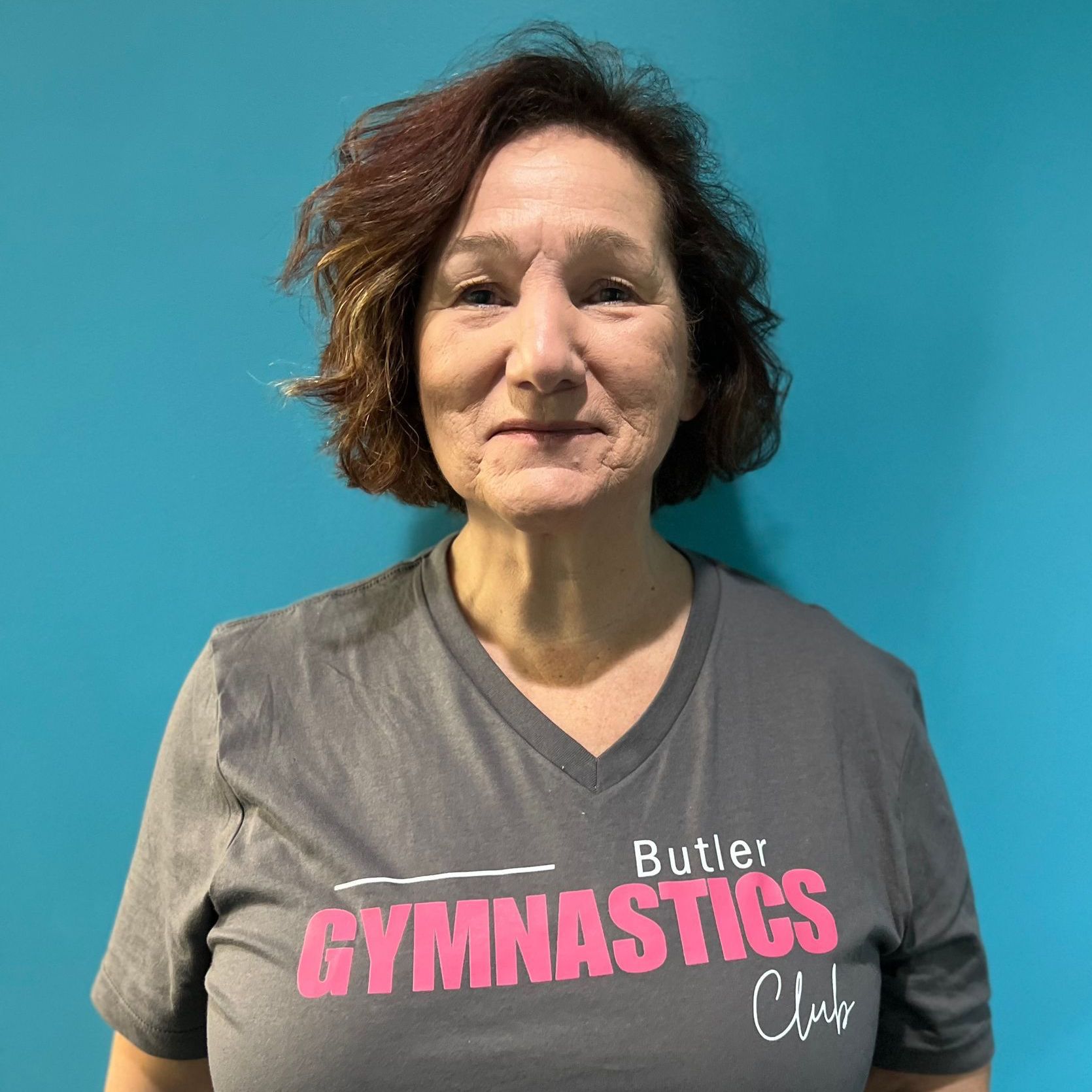 A woman wearing a butler gymnastics club t-shirt is standing in front of a blue wall.