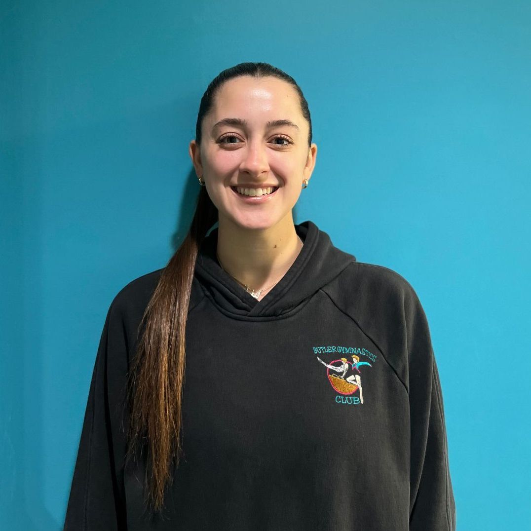 A woman wearing a black hoodie is smiling in front of a blue wall.