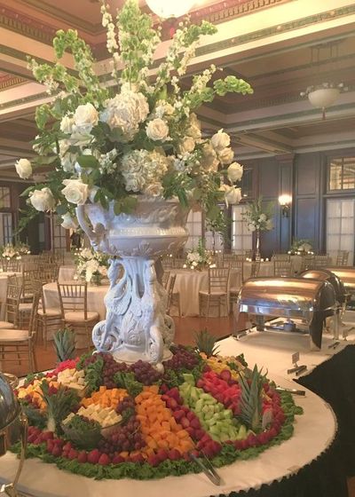A table with a vase of flowers and fruit on it.