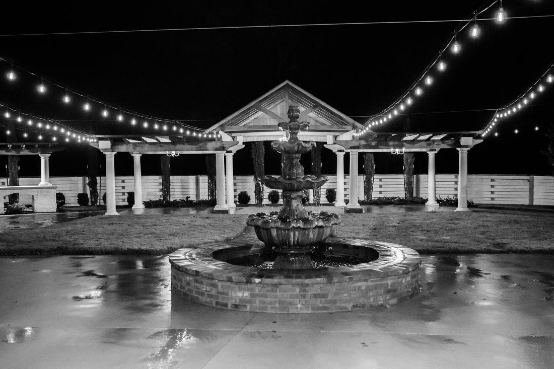 A black and white photo of a fountain in front of a building at night.
