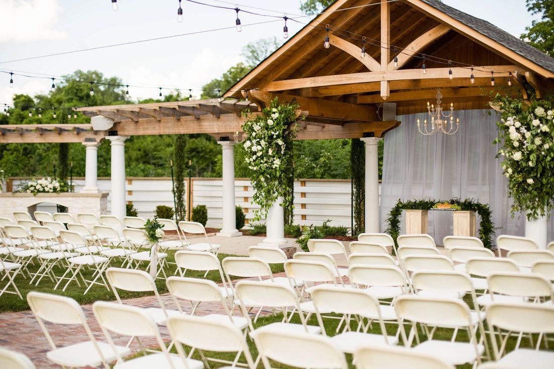 A row of white folding chairs are lined up in front of a wooden structure for a wedding ceremony.