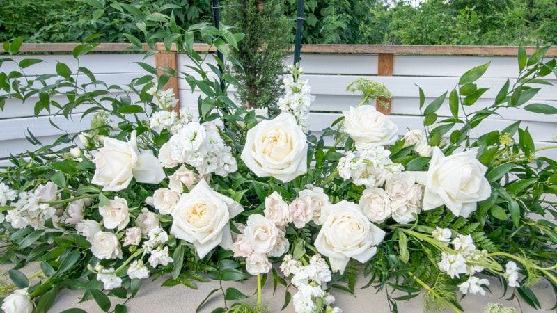 A table topped with lots of white flowers and greenery.