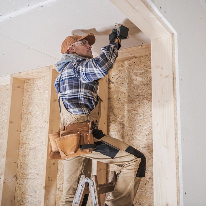 A man is sitting on a ladder working on a ceiling.