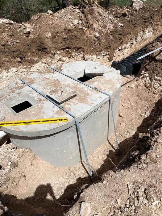 Concrete septic tank being installed in a trench, with pipes and soil visible.