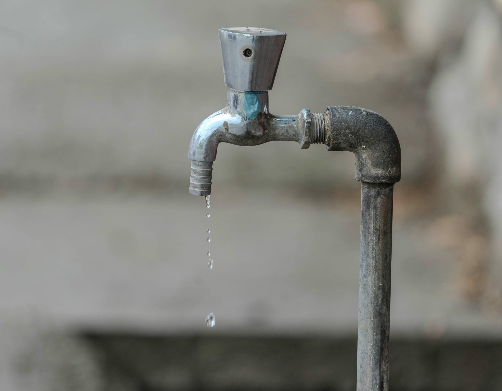 Dripping outdoor faucet, metal with water droplets falling. Blurred background.