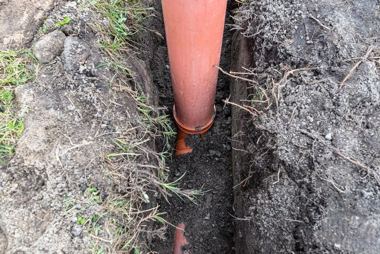 Orange pipe in a narrow trench dug in dirt and grass.