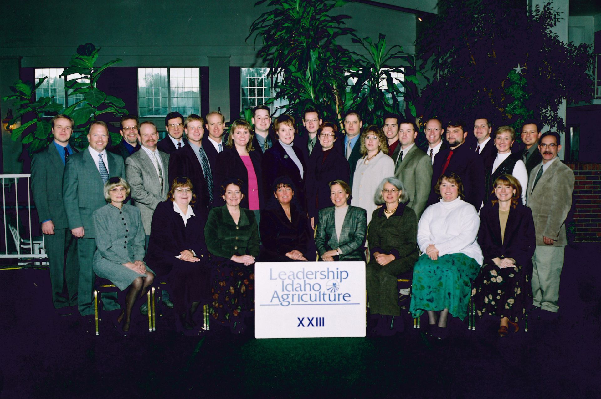 A group photo of Leadership Idaho Agriculture class XXII participants standing and sitting in a dark indoor space.