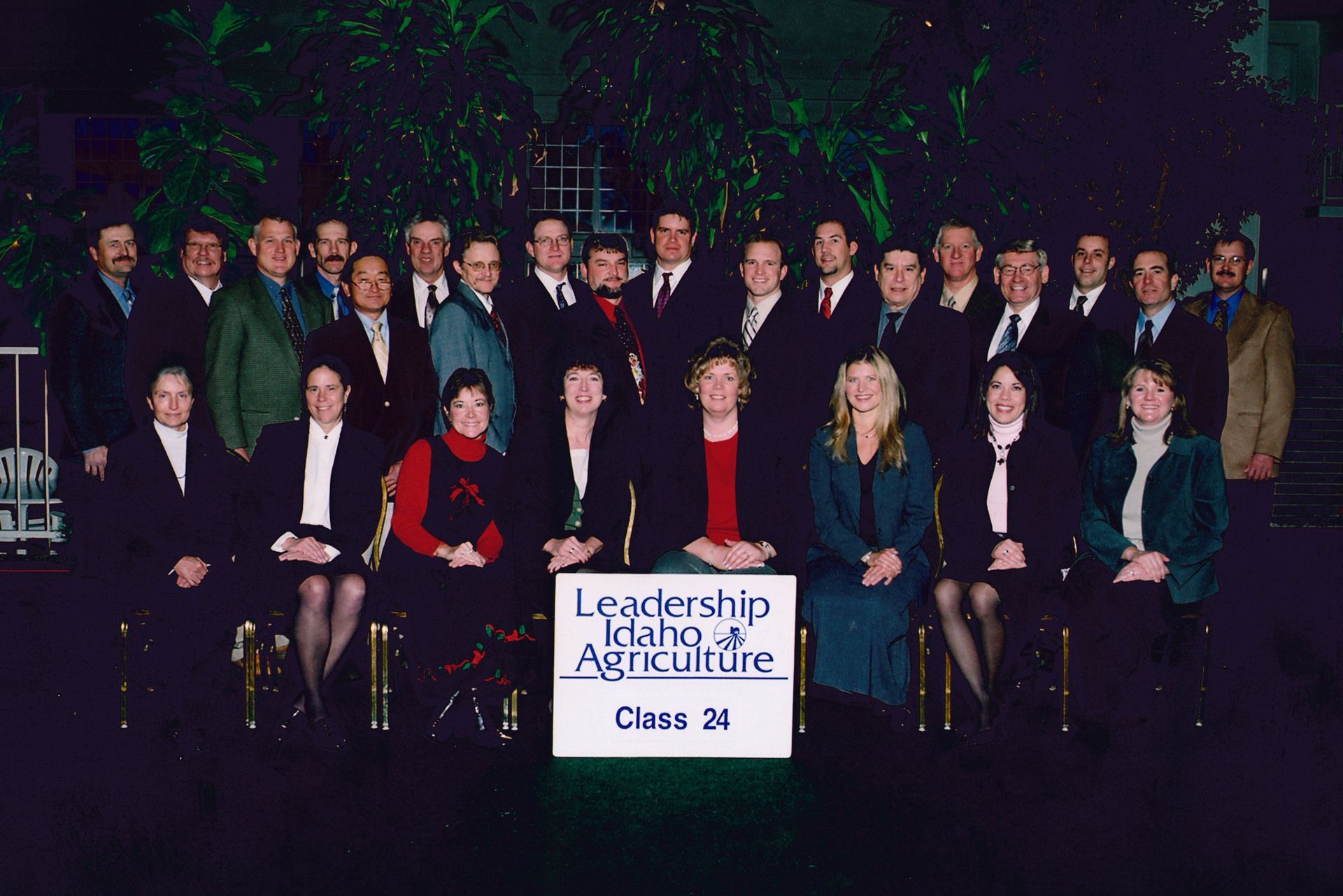 Group portrait of Leadership Idaho Agriculture Class 24 members posing in front of a sign and green foliage.