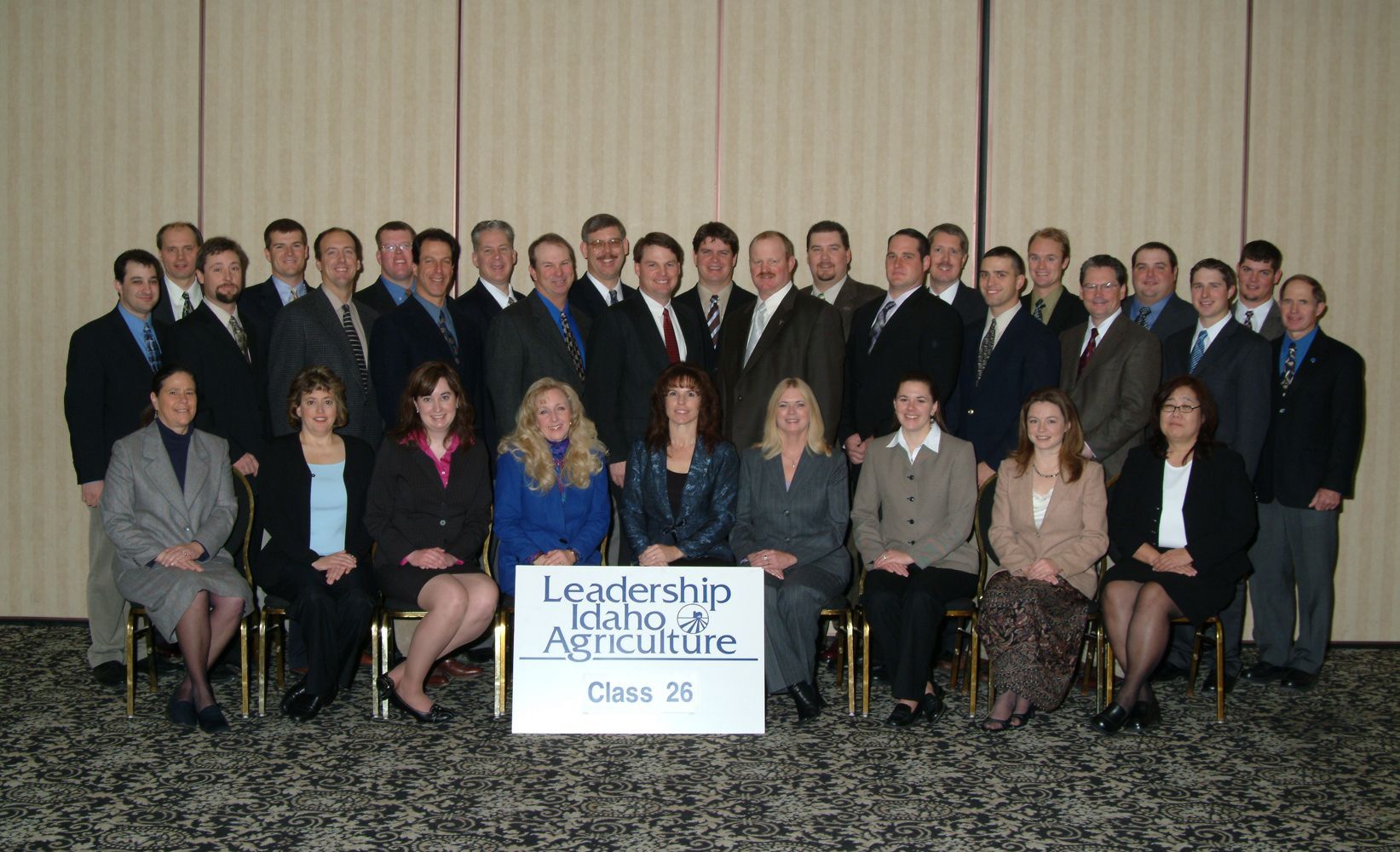 Class 26 of Leadership Idaho in Agriculture poses for a formal group portrait in a hotel conference room.
