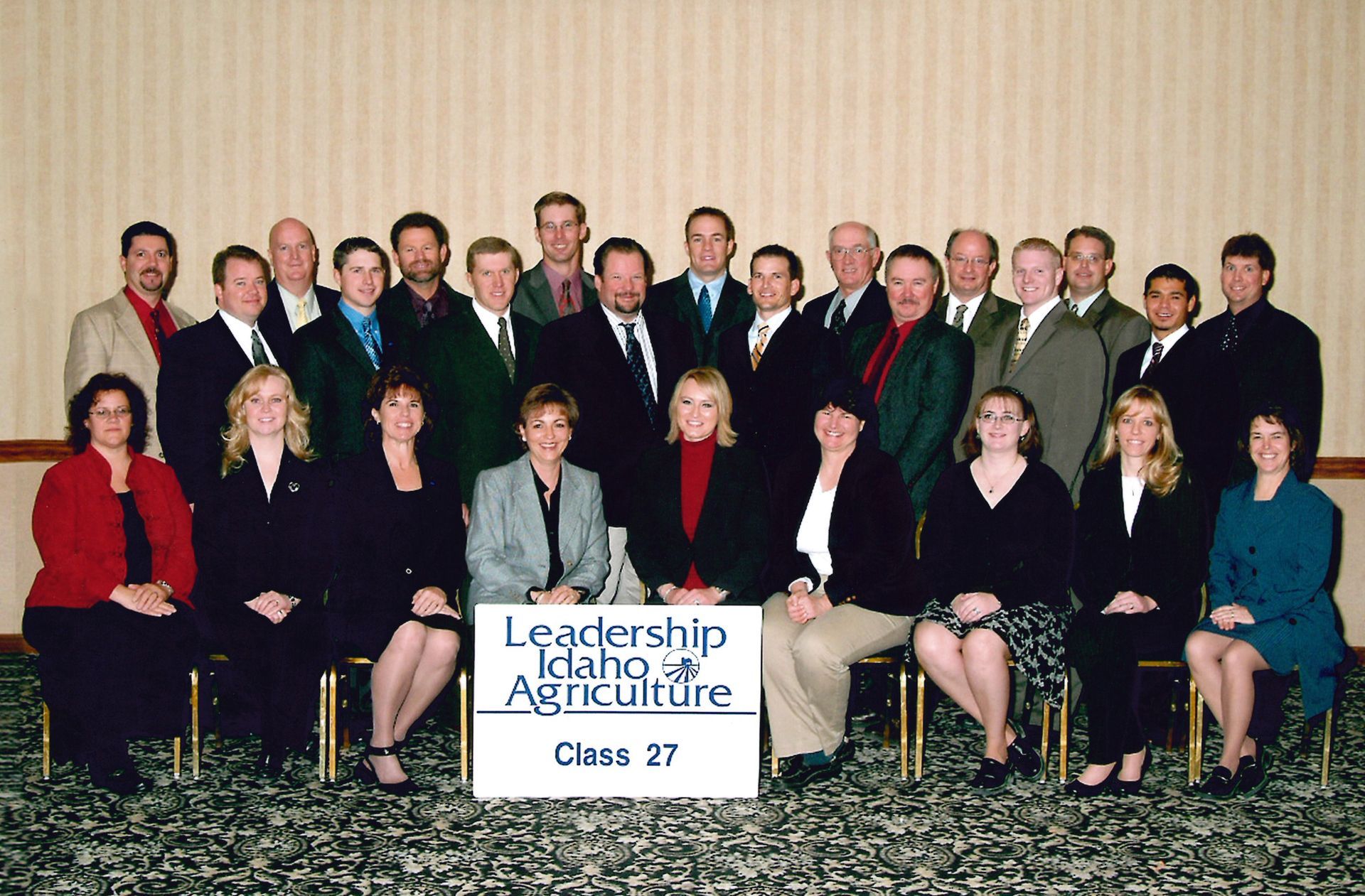 A formal group photo of the Leadership Idaho Agriculture Class 27, posing in two rows inside a room with patterned carpet.