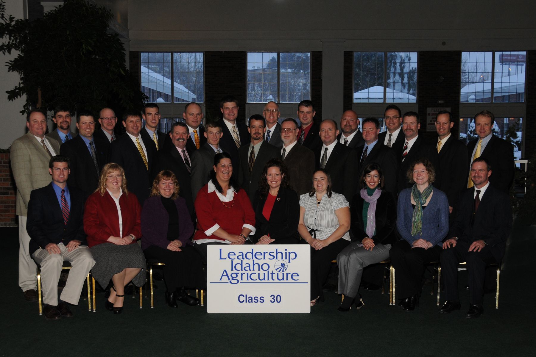 A group photo of Leadership Idaho Agriculture Class 50 members posing together with a sign in front of large windows.