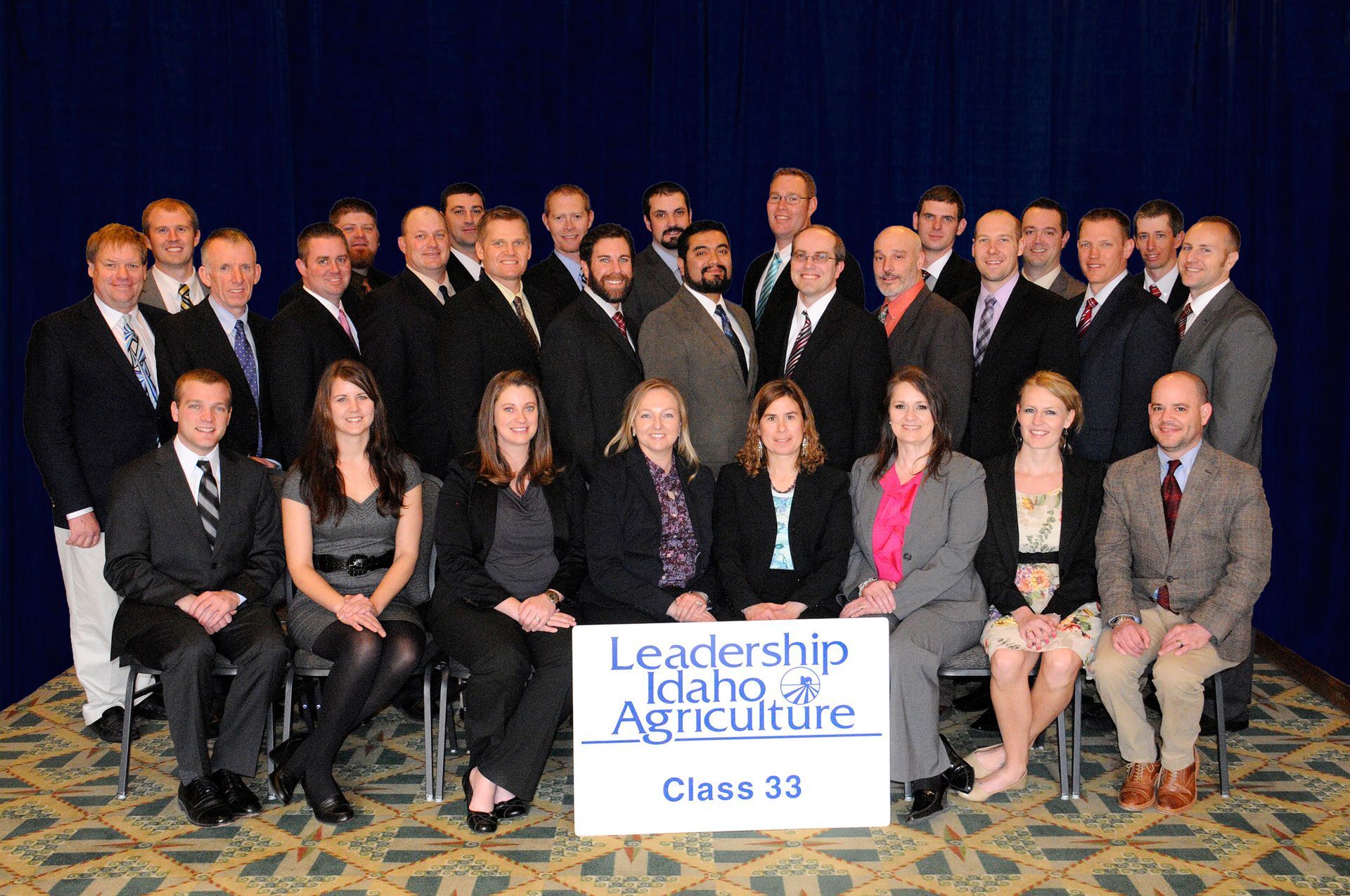 A large group posing for a Leadership Idaho Agriculture Class 33 graduation photo in front of a blue backdrop.