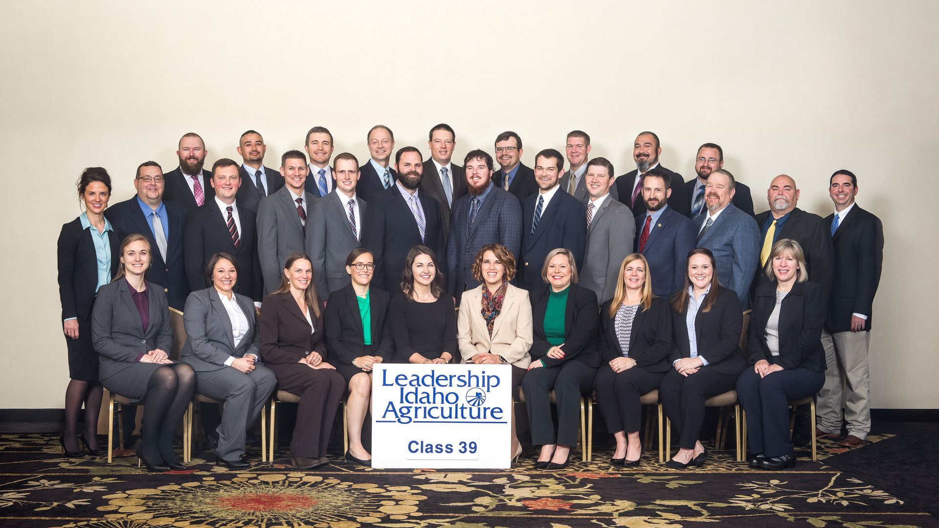 Group portrait of Leadership Idaho Agriculture Class 38 participants posing with a sign in a neutral-walled room.