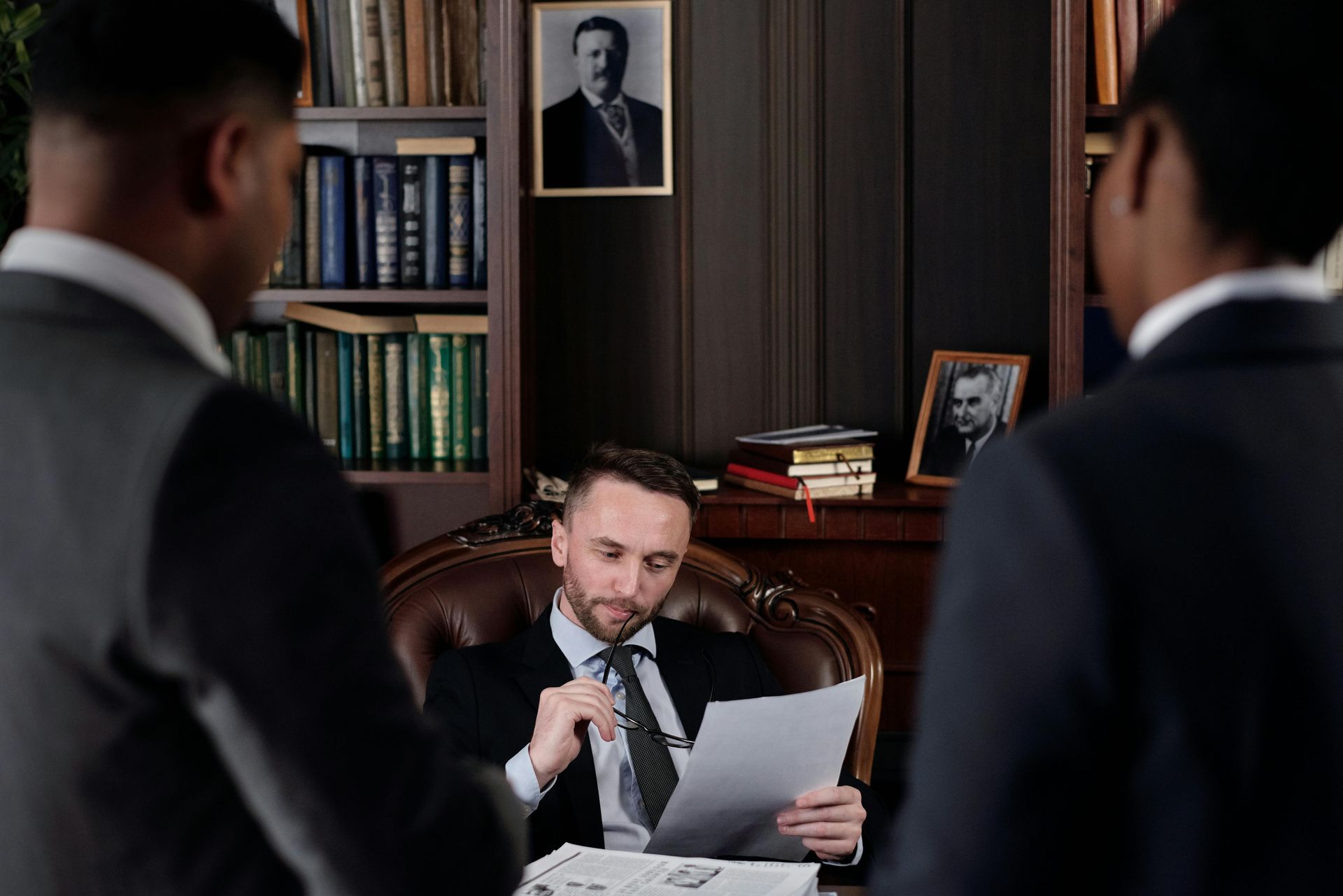 A man in a suit and tie is sitting at a table holding a piece of paper.