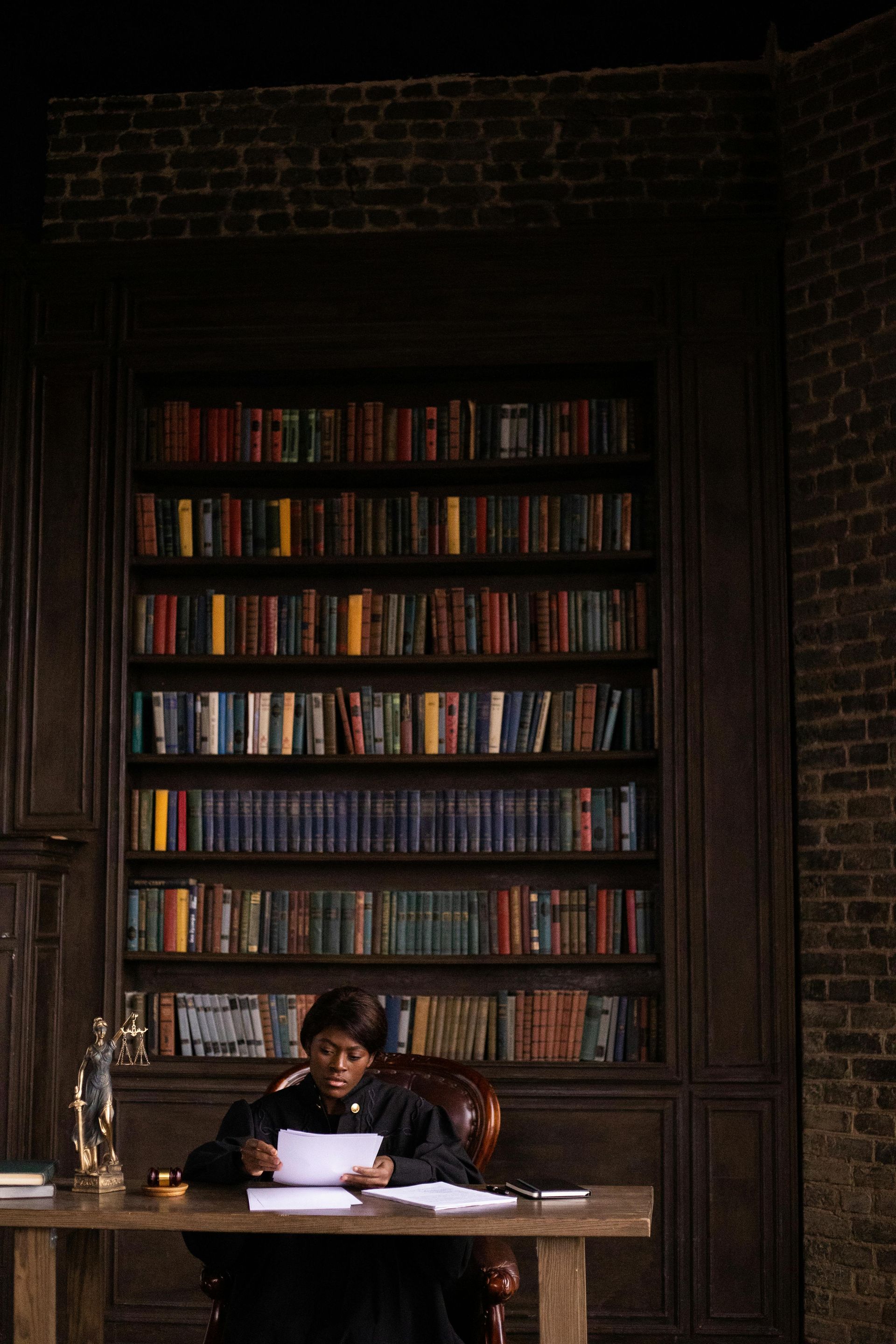 A man is sitting at a desk in a library reading a book.