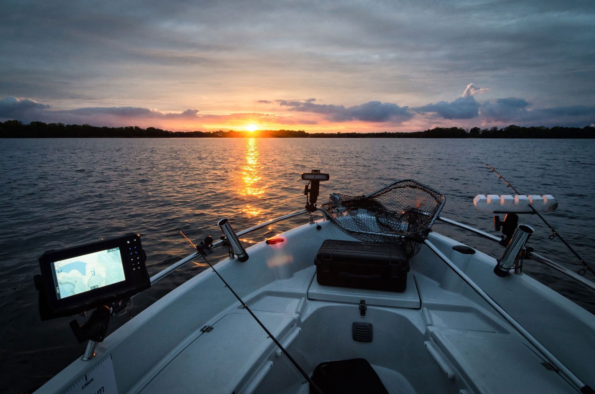 Fishing boat on calm water at sunset. Rods, net, and equipment on deck.