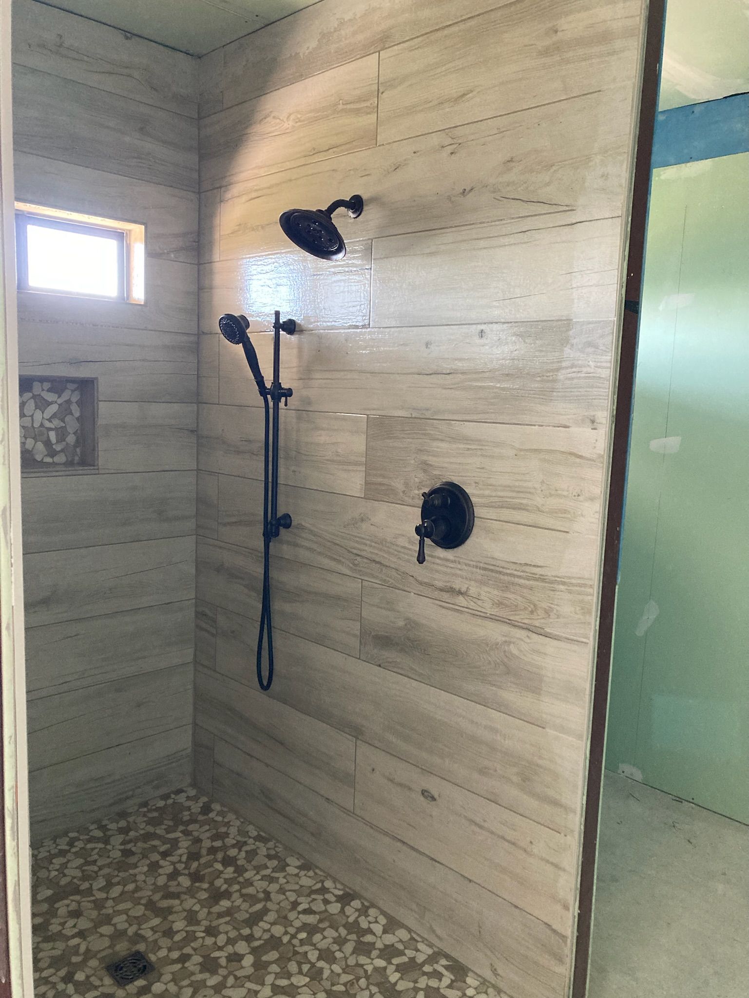 Shower with light stone tile walls, pebble floor, and black fixtures.