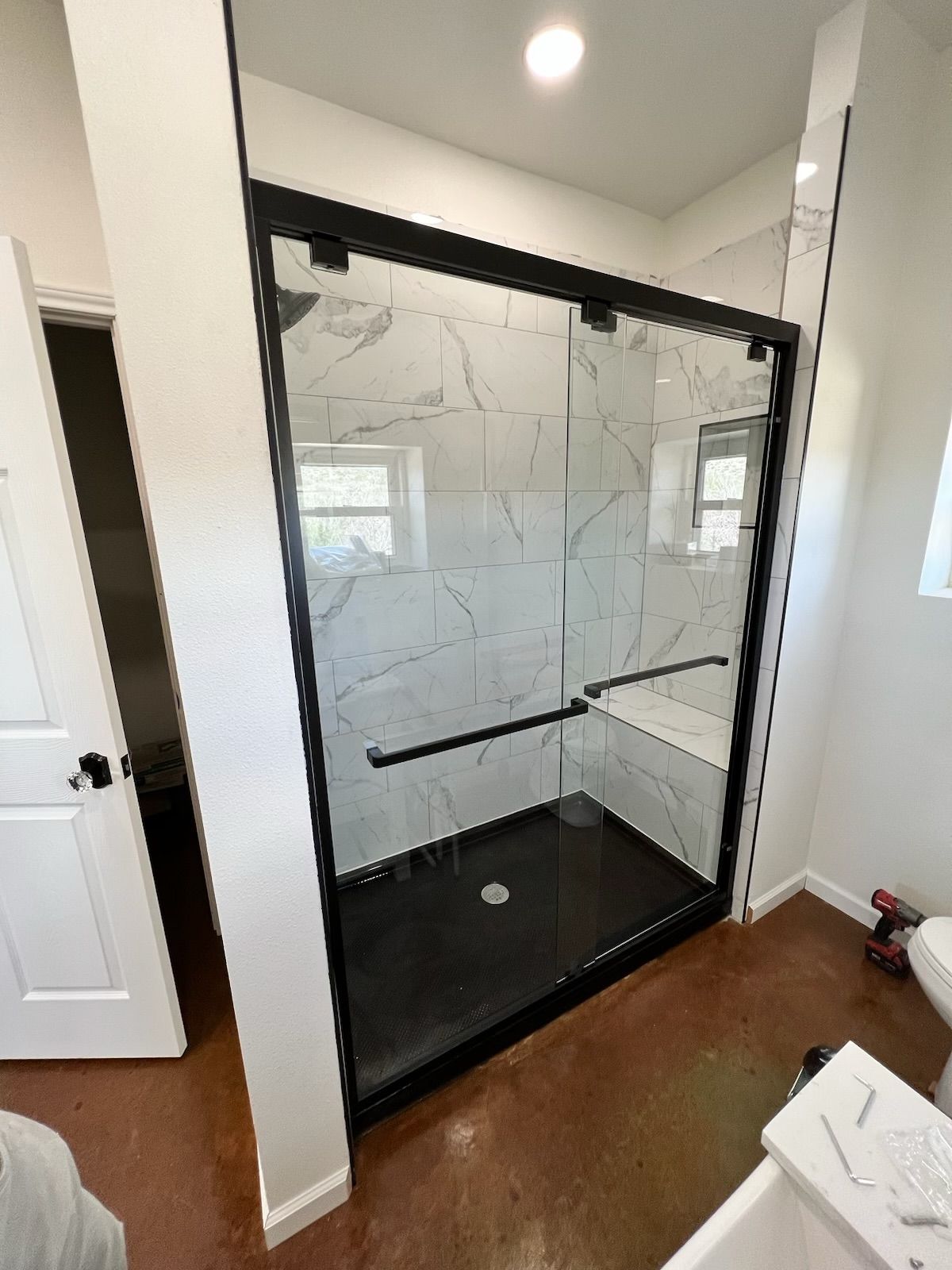 Black-framed glass shower with white marble tile walls, black base, and black hardware, in a bathroom.